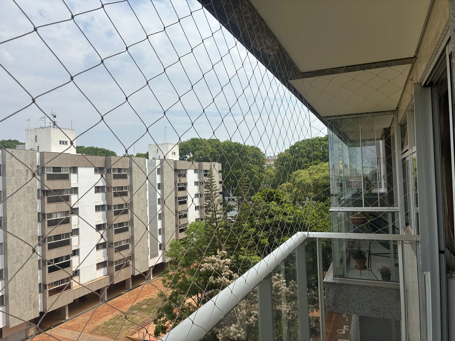 Vista lateral da rede areia na varanda, com os prédios e a vegetação ao fundo.