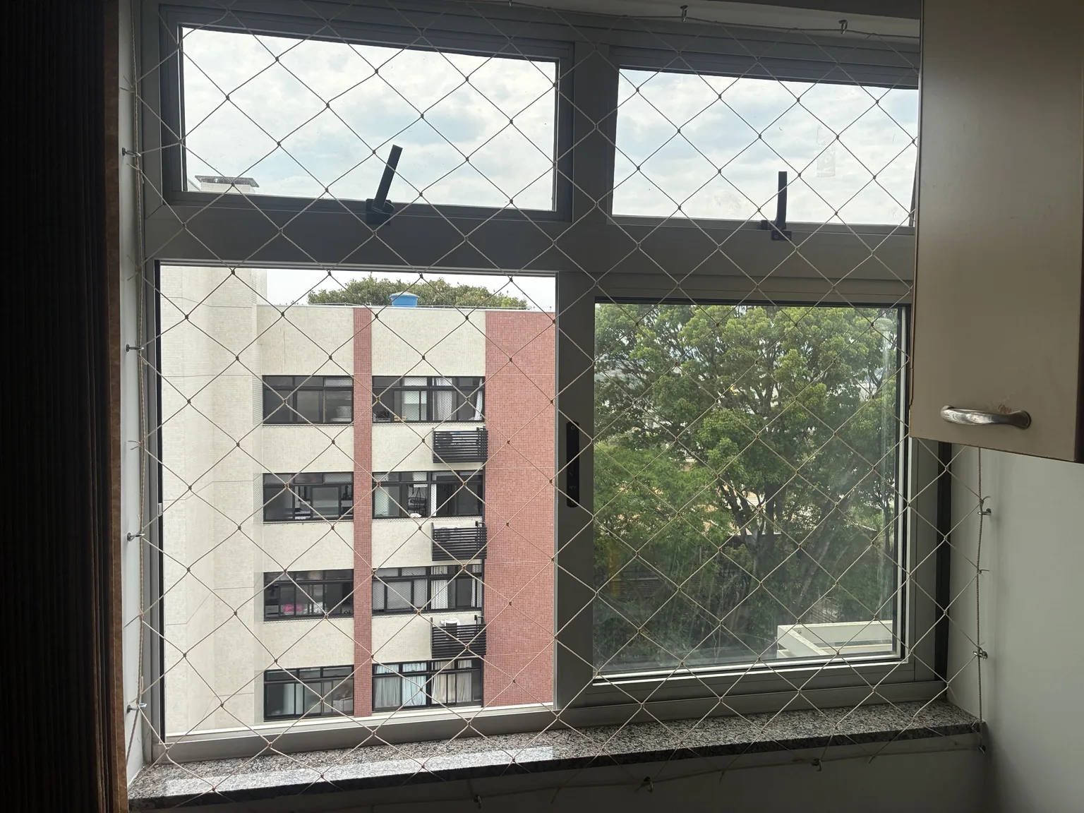Vista interna da janela com rede areia e folhas superiores basculantes.