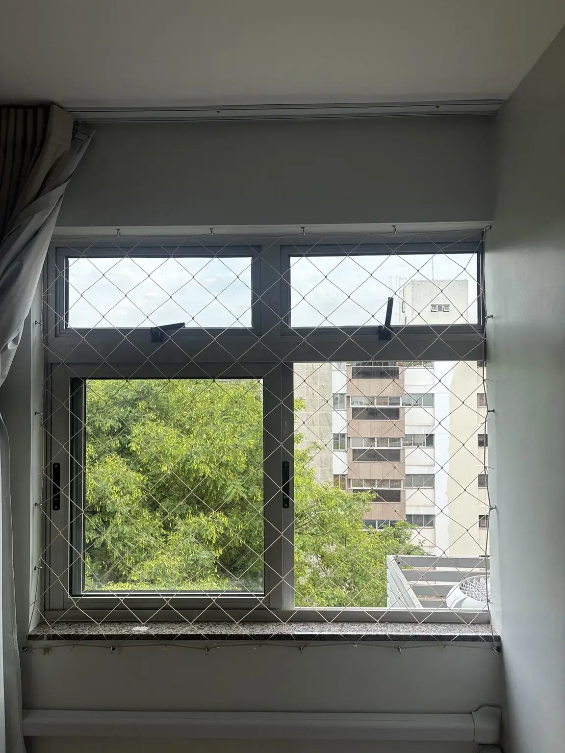 Rede areia diante da janela, com vista para a vegetação da quadra.