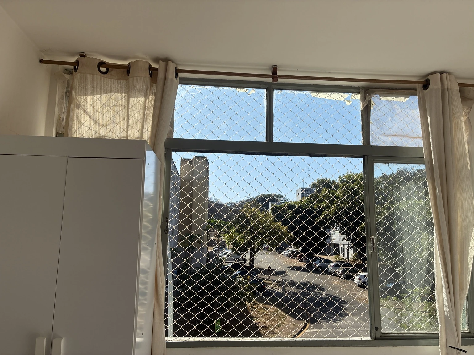 Rede de proteção 5×5 cm na cor areia em janela com cortinas claras na SQS 414, Bloco E, Asa Sul