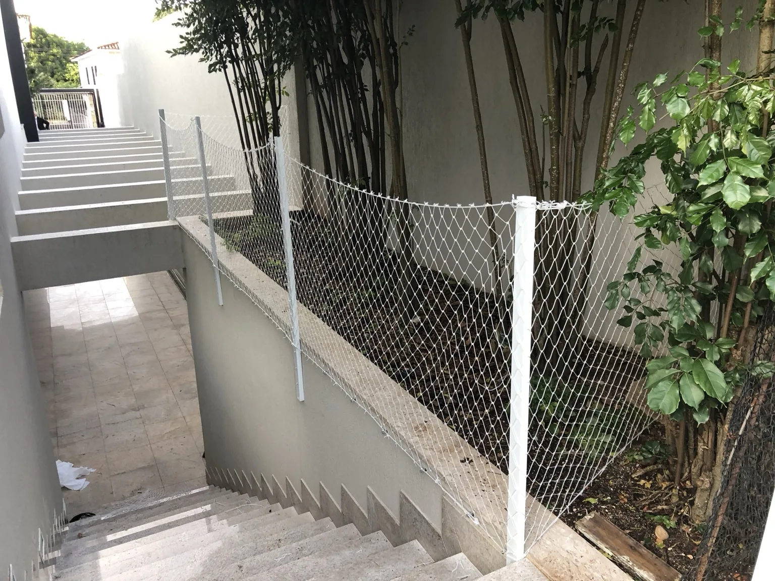 Rede branca instalada na borda de área externa ao lado de escada e jardim