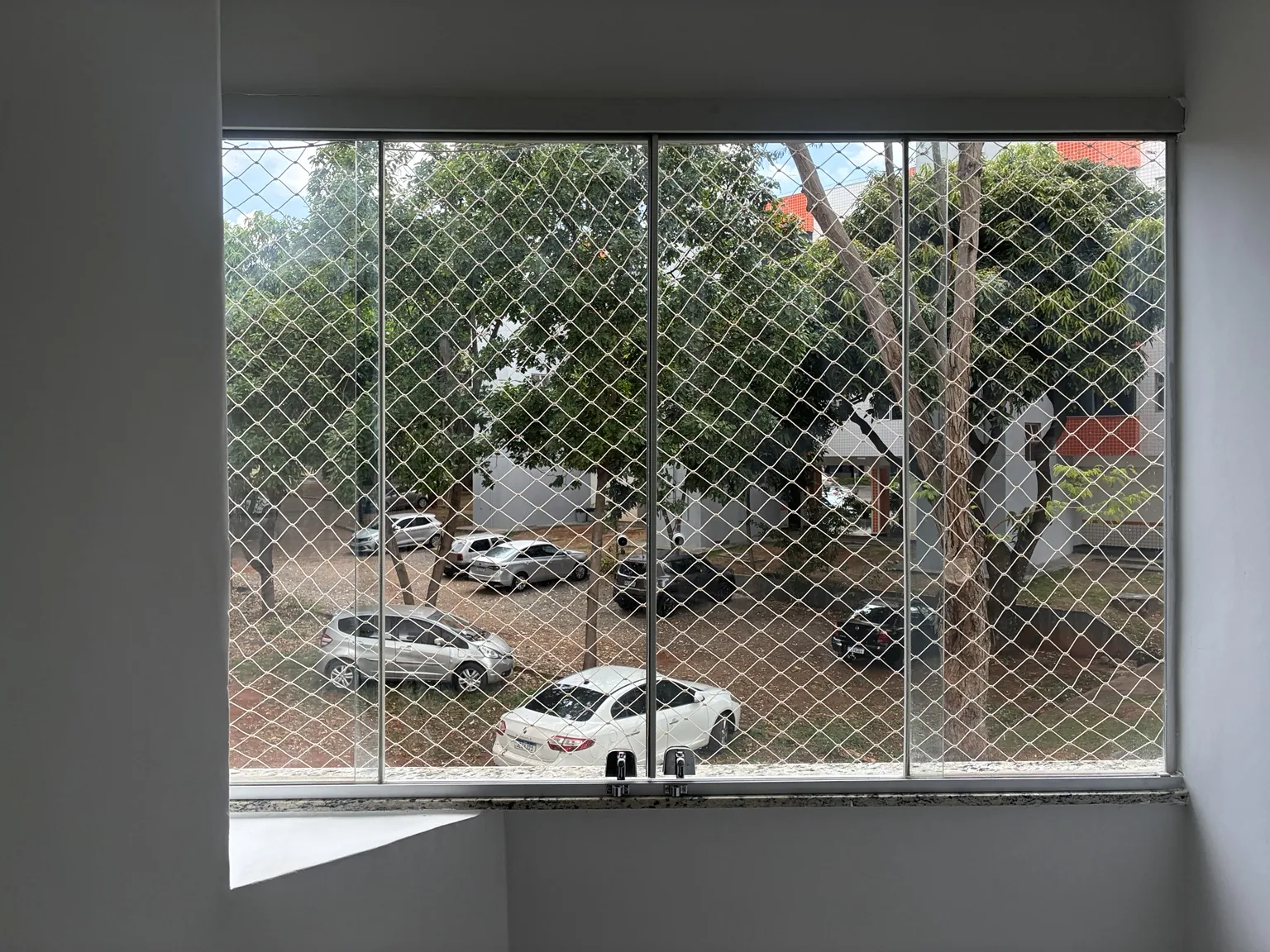 Rede areia instalada na janela, com vista para o estacionamento.