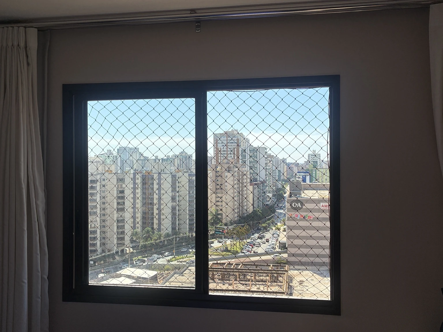 Janela protegida com rede de malha 5×5 cm, com vista para Águas Claras.