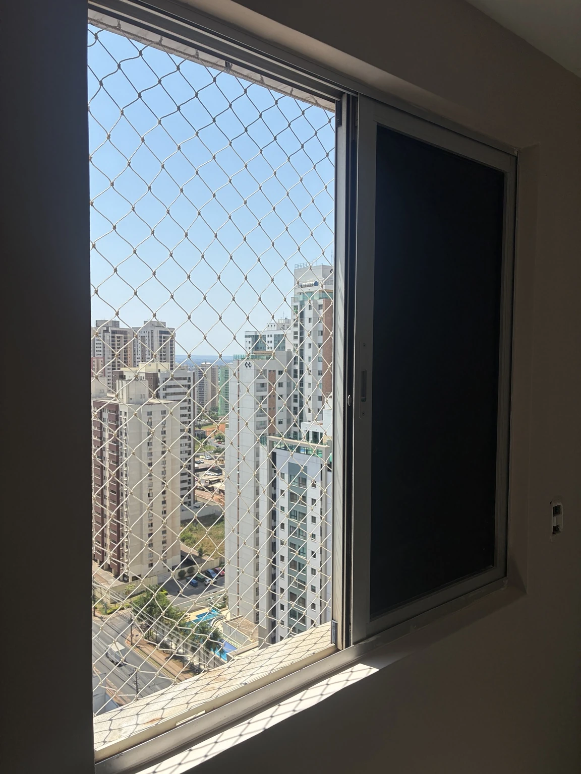 Rede areia 5×5 cm na abertura da janela com edifícios ao fundo no Ed. Spetaculo Clube Residencial, Avenida Sibipiruna, Águas Claras
