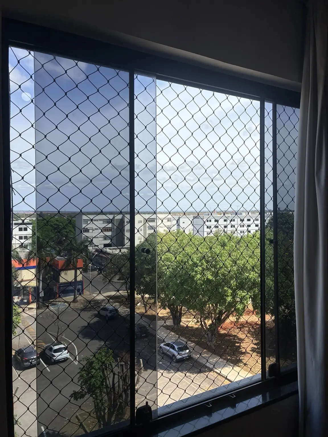 Detalhe da rede preta acompanhando a janela e a vista externa do Cruzeiro Novo.