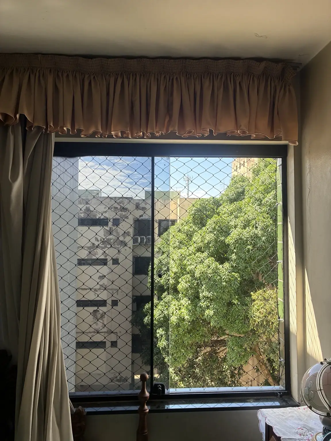 Janela com cortinas protegida com rede de malha 5×5 cm na cor preta.