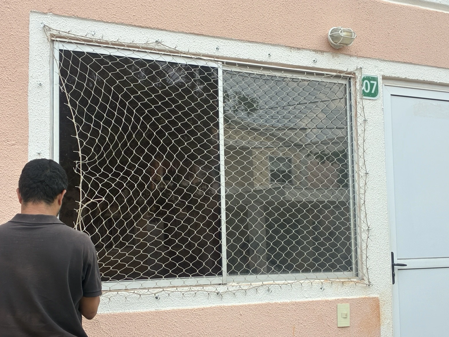 Etapa de posicionamento da rede de proteção na janela da QC 9, Rua B, no Jardins Mangueiral