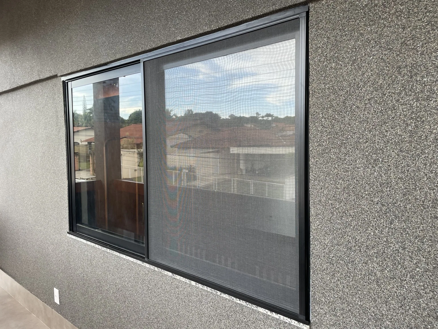 Janela de correr com tela mosquiteira preta vista pelo exterior da embaixada