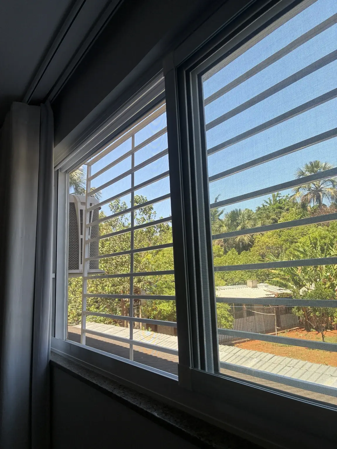 Detalhe da tela mosquiteira com acabamento branco junto à janela e à grade externa.