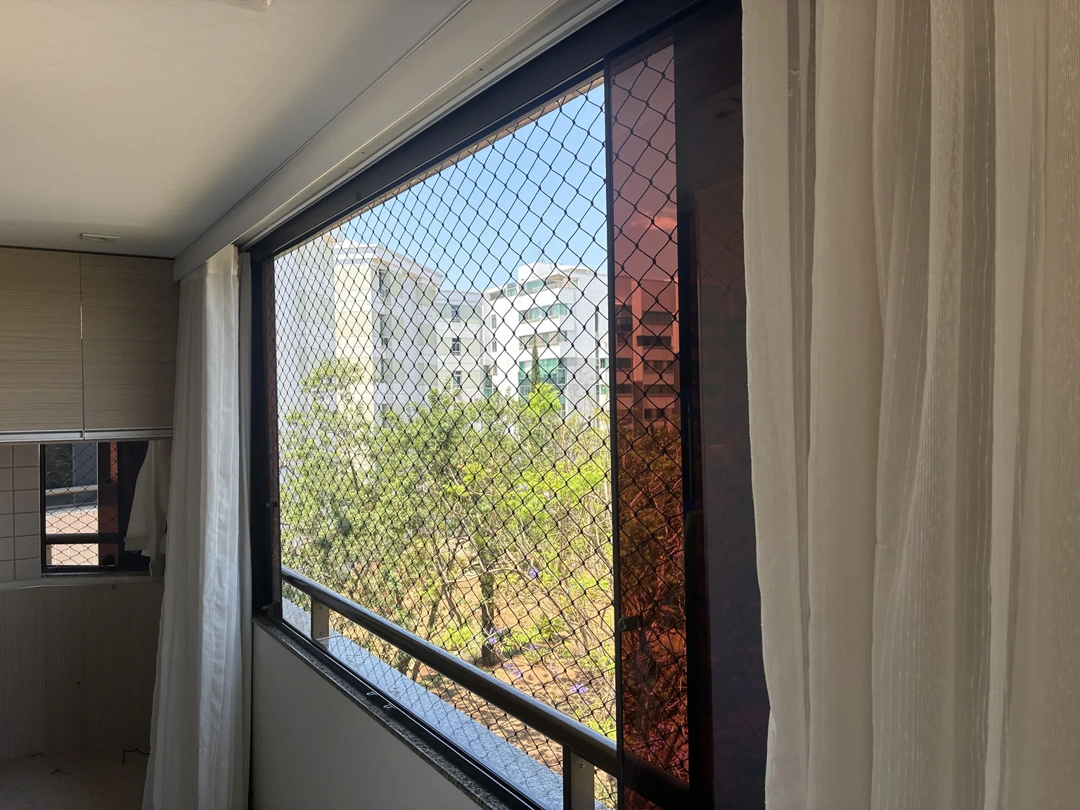 Janela com rede de proteção preta e vista externa no Edifício Porto Parati